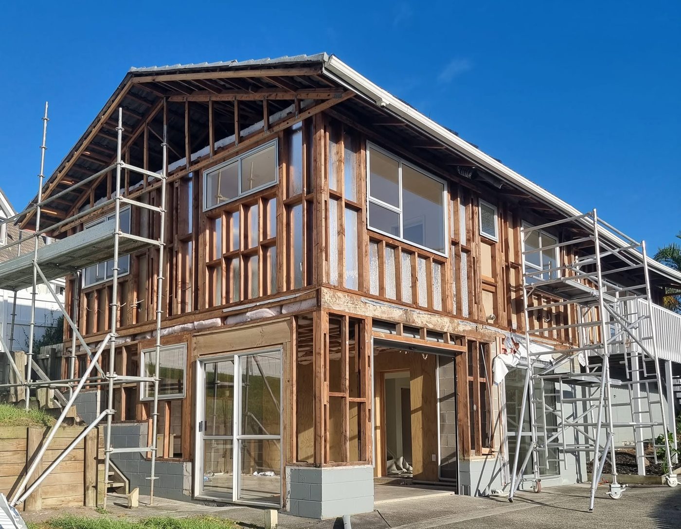 Two-storey house with asbestos cladding stripped back to framing under scaffold